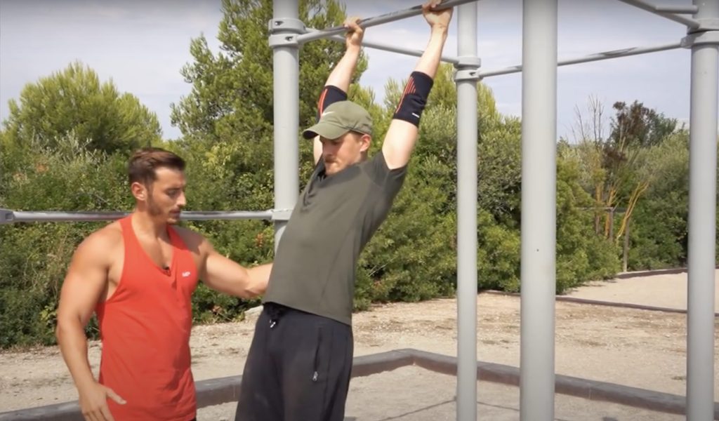 Homme se balançant sur une barre de traction pour réussir le muscle, aidé par son coach sportif