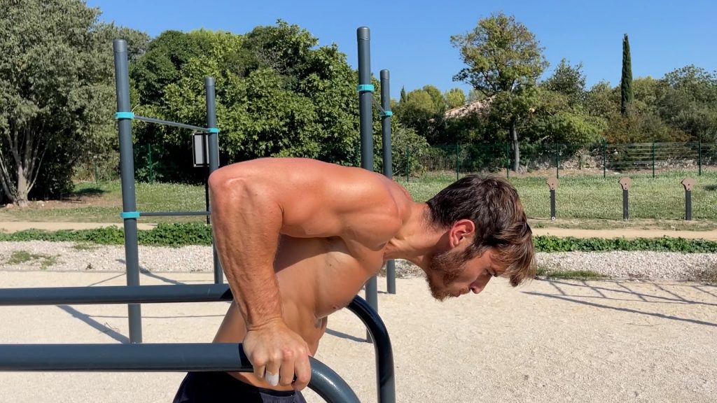 Homme faisant des dips sur des barres parallèles dans un parc de Street Workout en phase de descente du mouvement