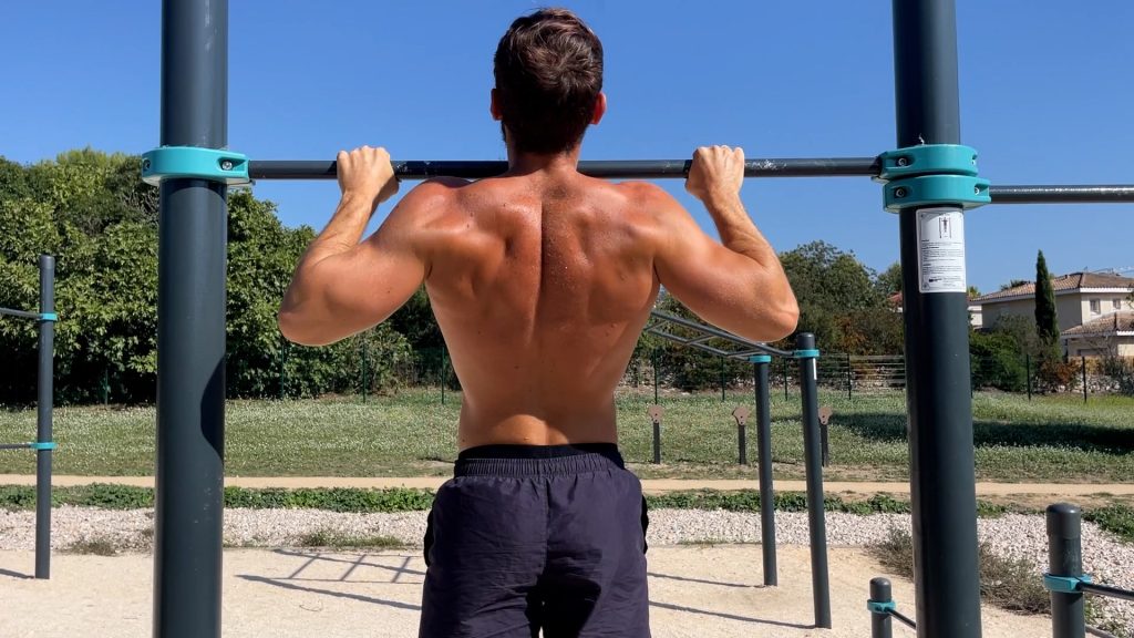Homme de dos faisant des tractions avec la tête au-dessus de la barre dans un parc de Street Workout