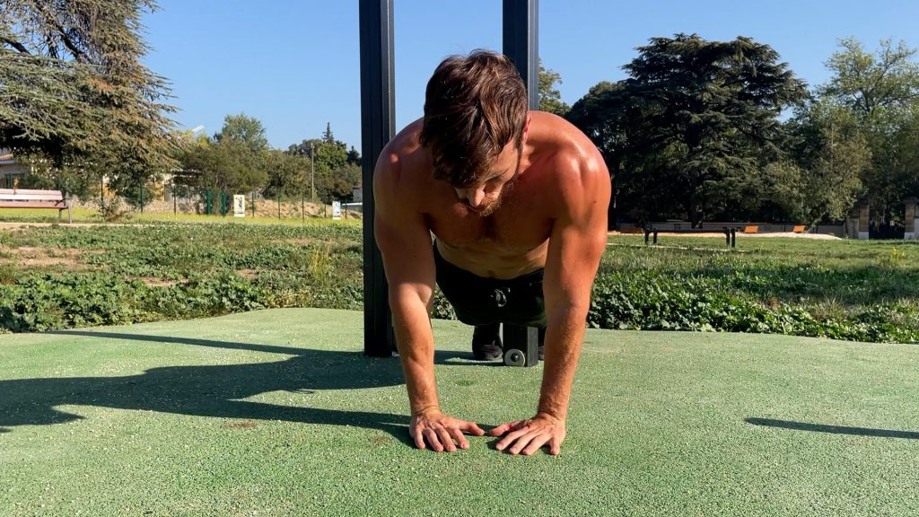 Homme faisant des pompes prises serrées dans un parc de Street Workout en début de mouvement