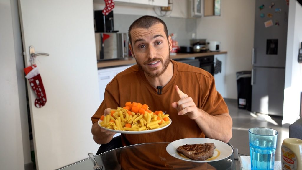 Homme montrant un plat de pâtes avec un steak à côté pour son déjeuner
