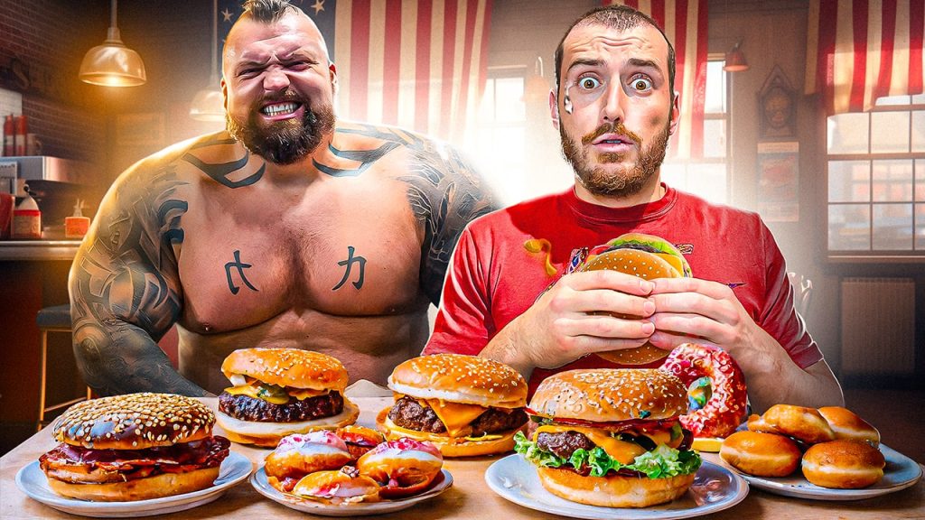 Homme en train de manger un burger avec d'autres assiettes de nourriture "junk food" devant lui et un Strongman en fond