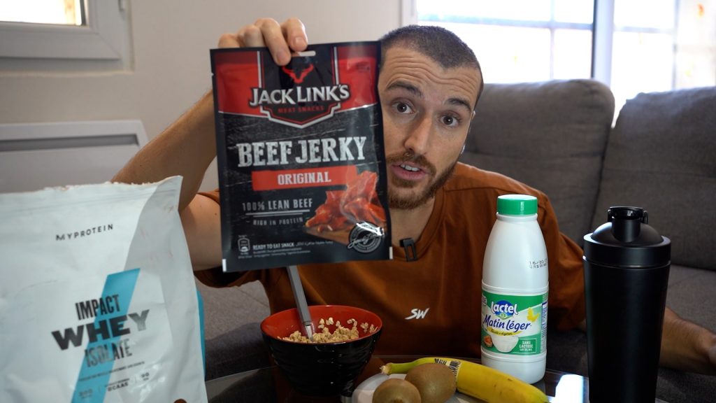 Homme montrant un sachet de bœuf séché avec un bol d'avoine, de la protéine en poudre, du lait et des fruits à côté pour son second petit déjeuner