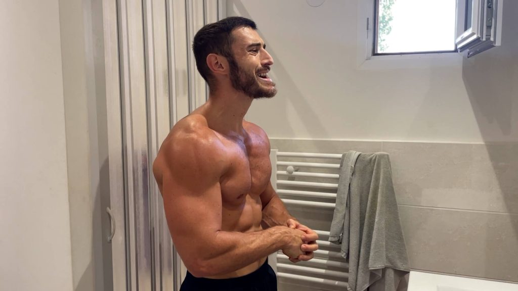 Homme de profil dans une salle de bain qui contracte ses muscles