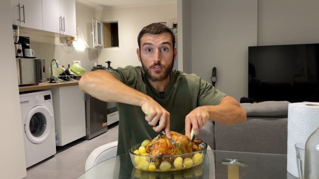 Homme sportif en train de couper un poulet entier dans un plat pour le manger, avec des pommes de terre