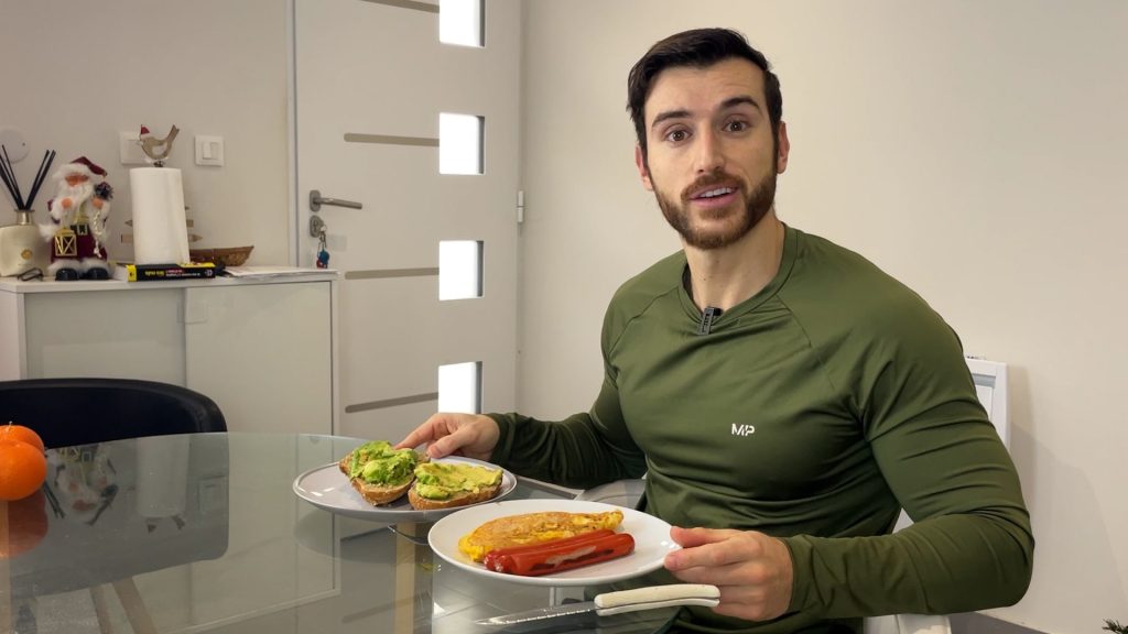 Homme assis avec le sourire prêt à manger son petit-déjeuner avec des œufs, des saucisses et des toasts à l'avocat