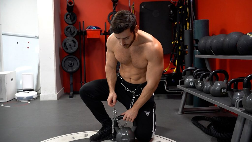 Homme dans une salle de sport en train d'attacher un kettlebell autour de sa taille à l'aide d'une ceinture de lest