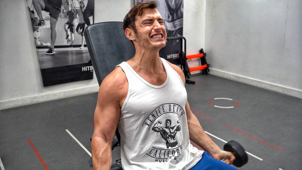 Homme assis sur un banc dans une salle de sport en train d'effectuer des curl biceps aux haltères